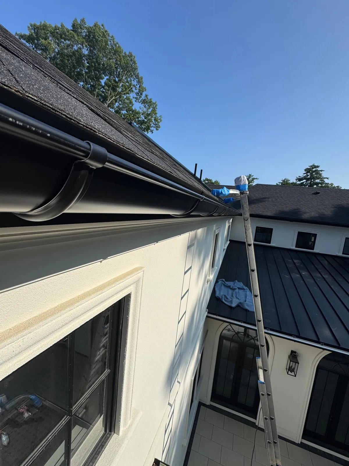Looking along a dark gutter run on a shingled eave toward a metal roof section