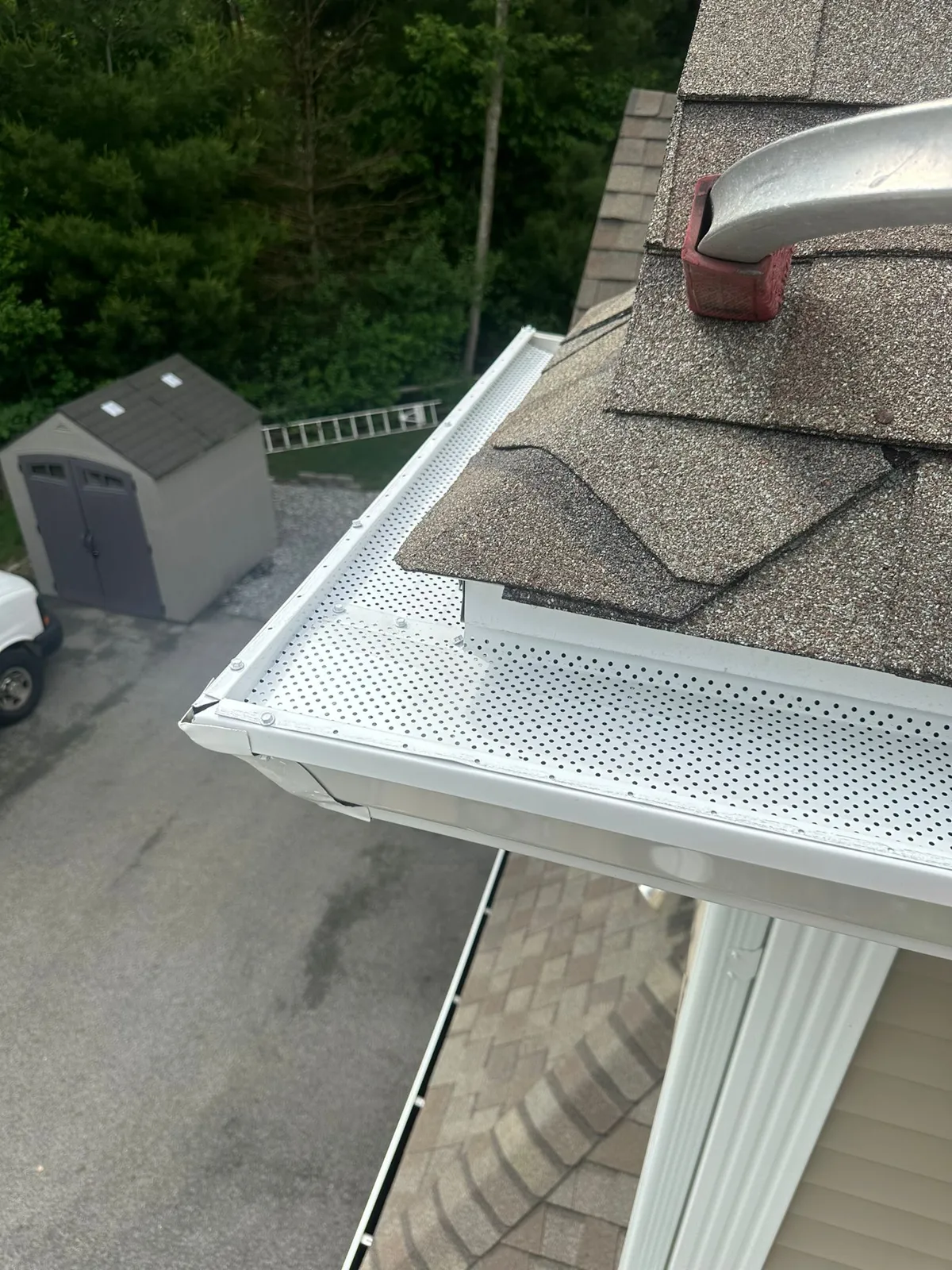 White gutter with a perforated guard along a shingled roof edge