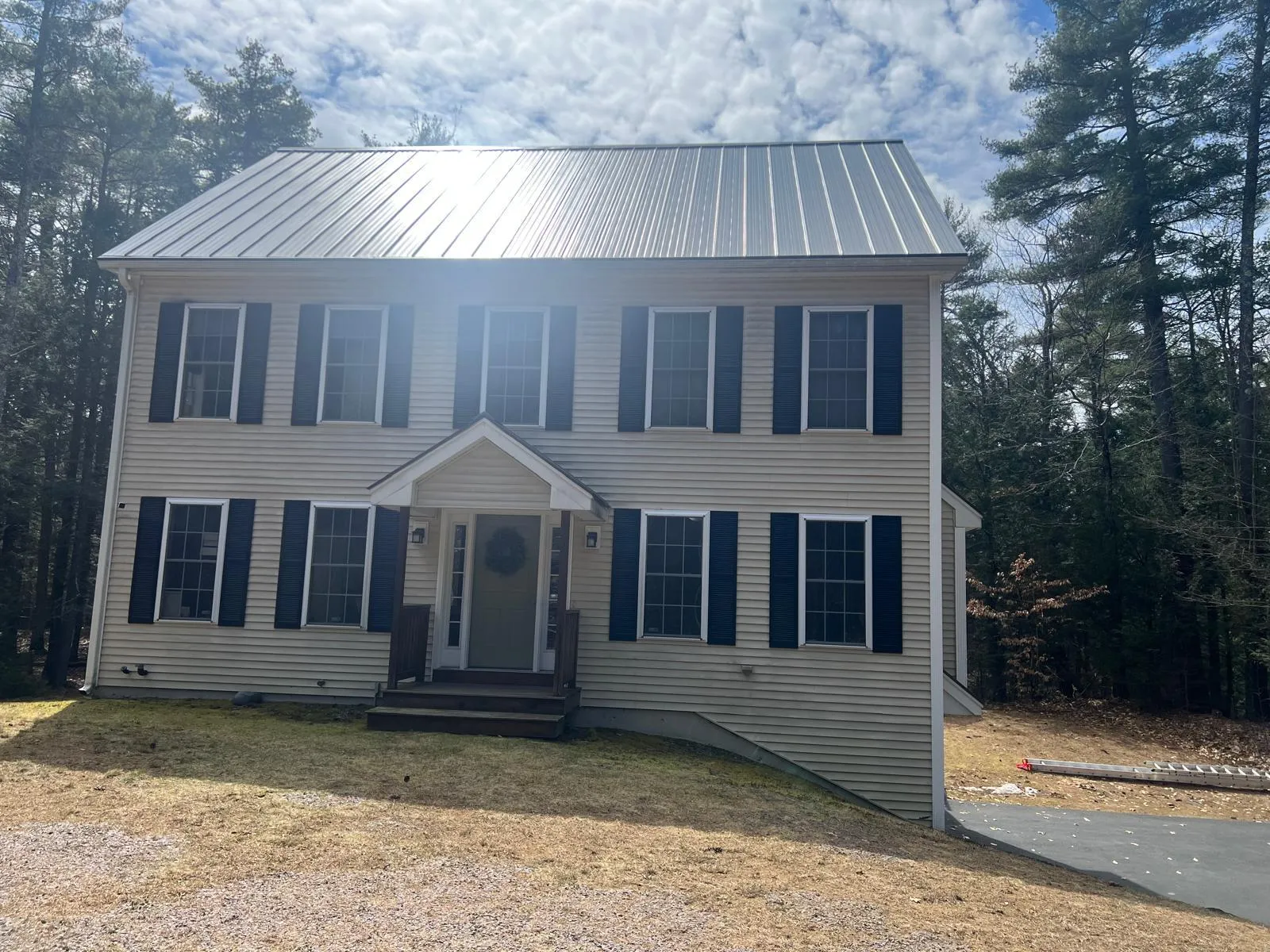 Two-story colonial with a full silver standing seam metal roof and dark shutters