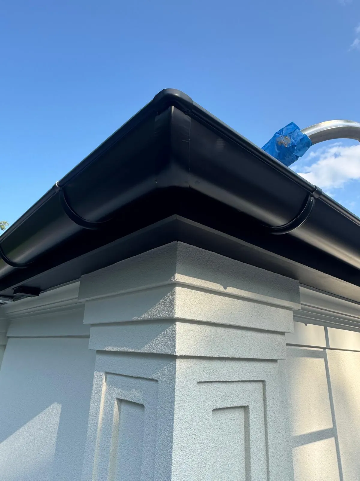 Close-up of a dark gutter wrapping an outside corner above white trim