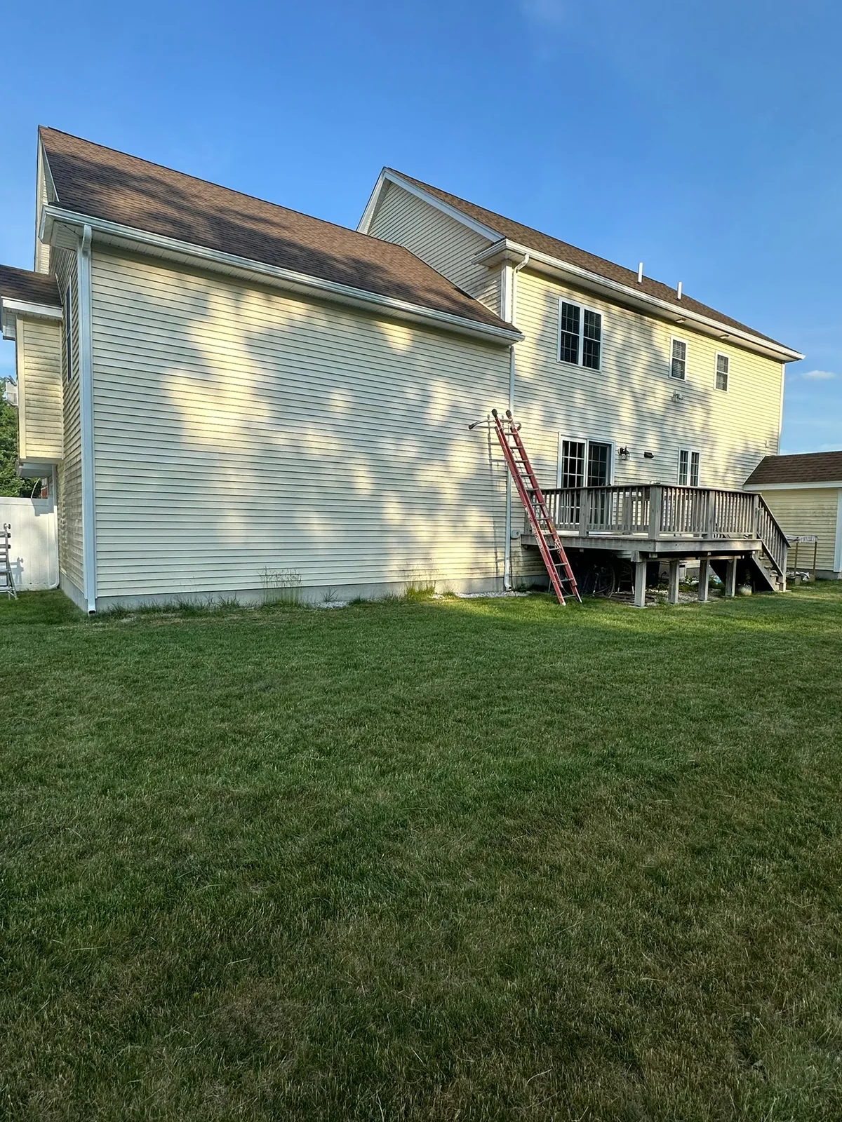 Light-sided house with ladders along a shingled residential roofline